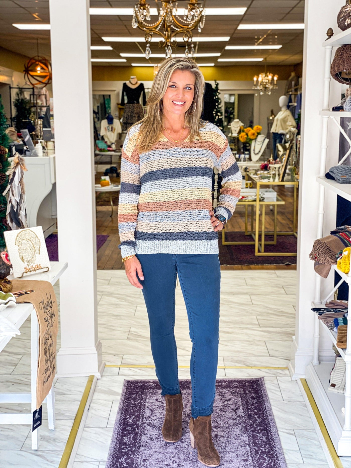 Model wearing fall fashion outfit that features an open-knit striped sweater with v-neck and long sleeves paired with balsam blue colored denim pants with frayed edge hem details from Charlie B.