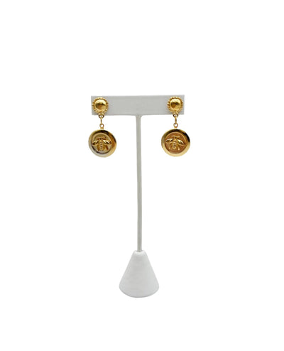 Gold bee locket drop earrings on a white display