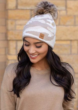 Tan camo knit beanie with cuff and faux fur pom on model front view.